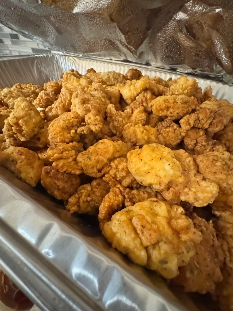 Golden-brown fried chicken bites, seasoned with herbs, fill a large aluminum catering tray.