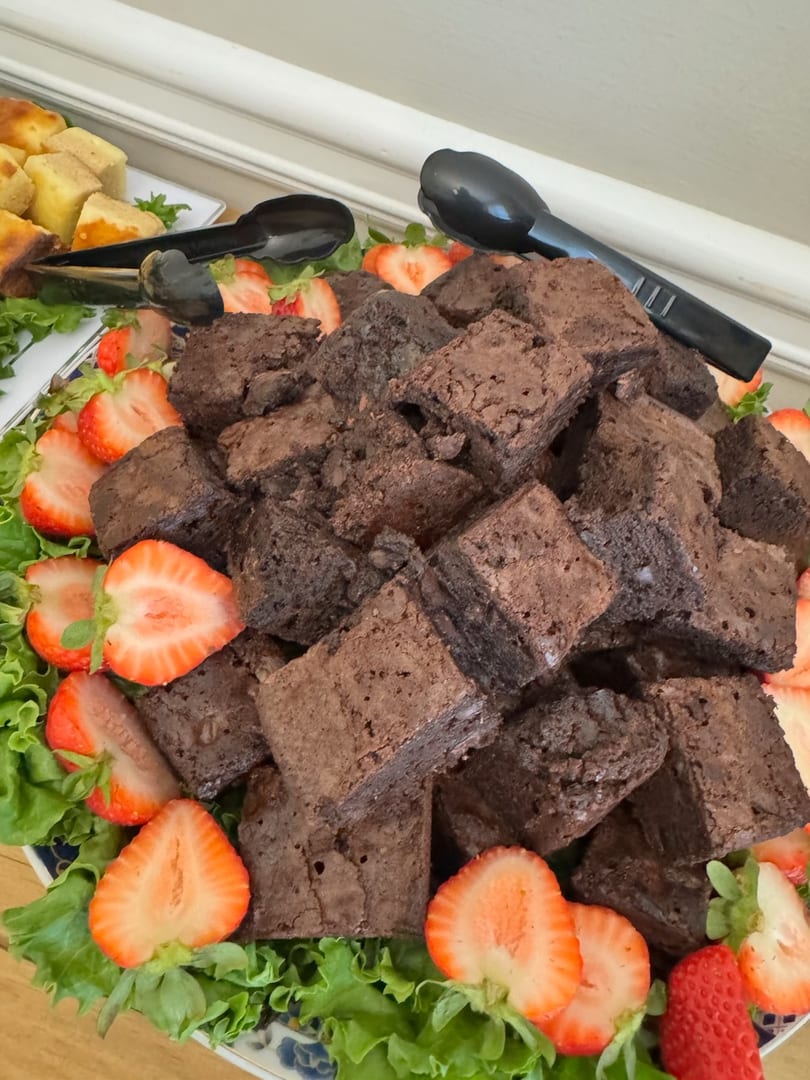 A platter of brownies and sliced strawberries on a bed of lettuce with serving tongs.