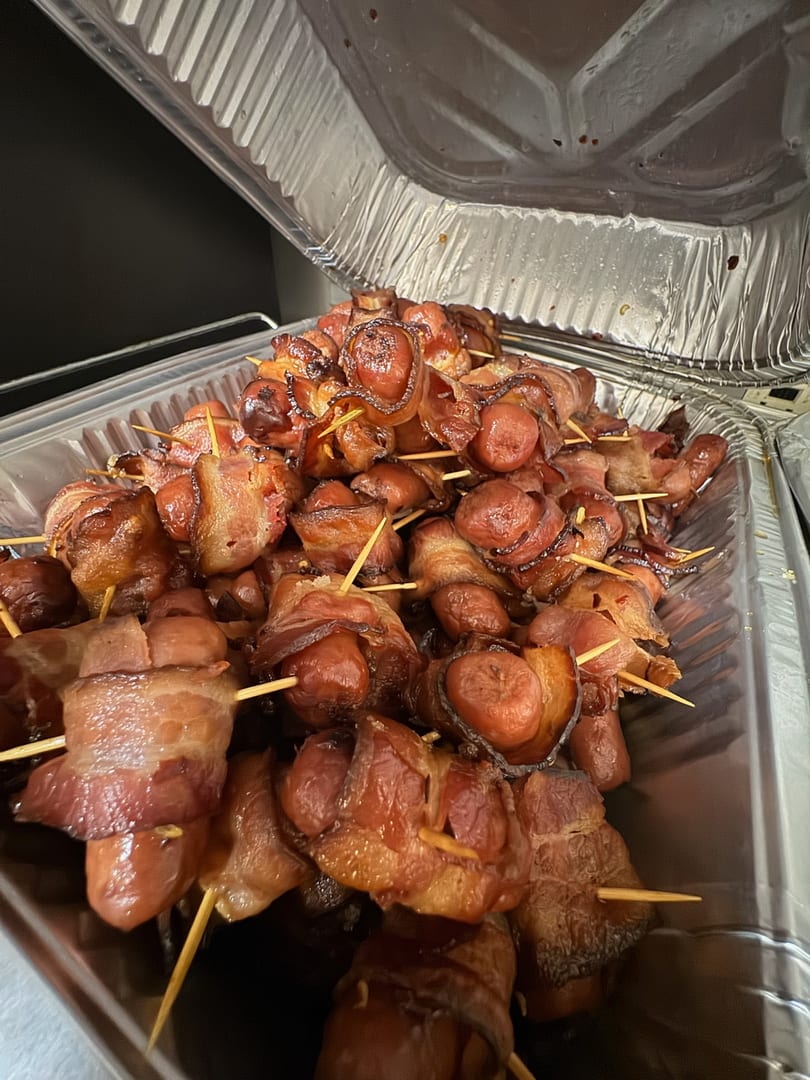 A foil tray filled with numerous bacon-wrapped hot dogs, each secured with a toothpick.